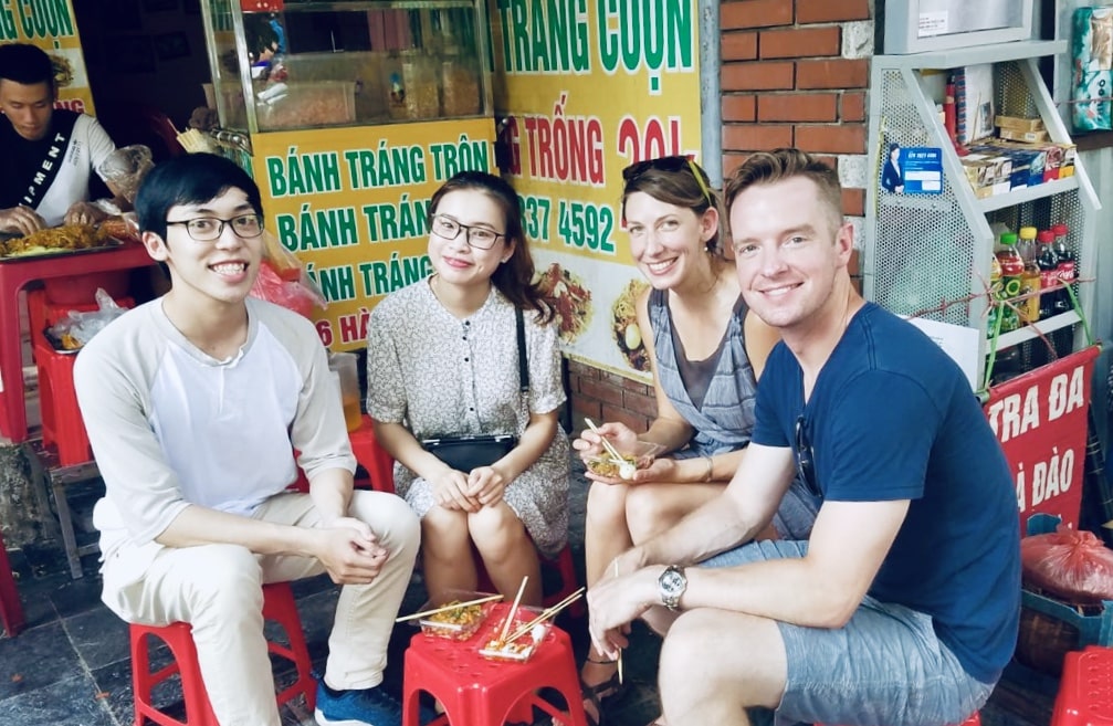 Kelsey and Nate eating Bánh Tráng Trôn, a rice paper, mango, and dried beef liver salad topped with a quail egg, with language tutor Cô Phướng Anh and her partner Đuc on the street in Hanoi.